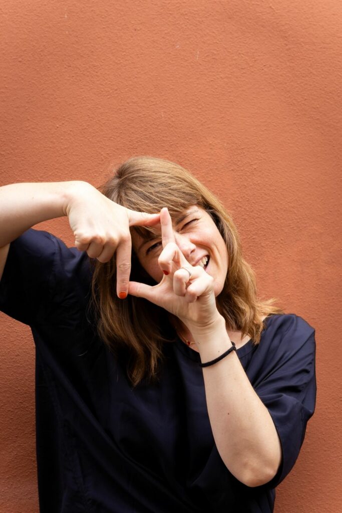 Portrait photo of Rosien against a wall, making a frame with her fingers and looking through it