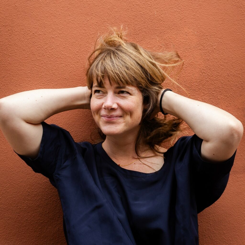 Portrait photo of Rosien against a wall, smiling, hands on the back of my head, windblown hair.